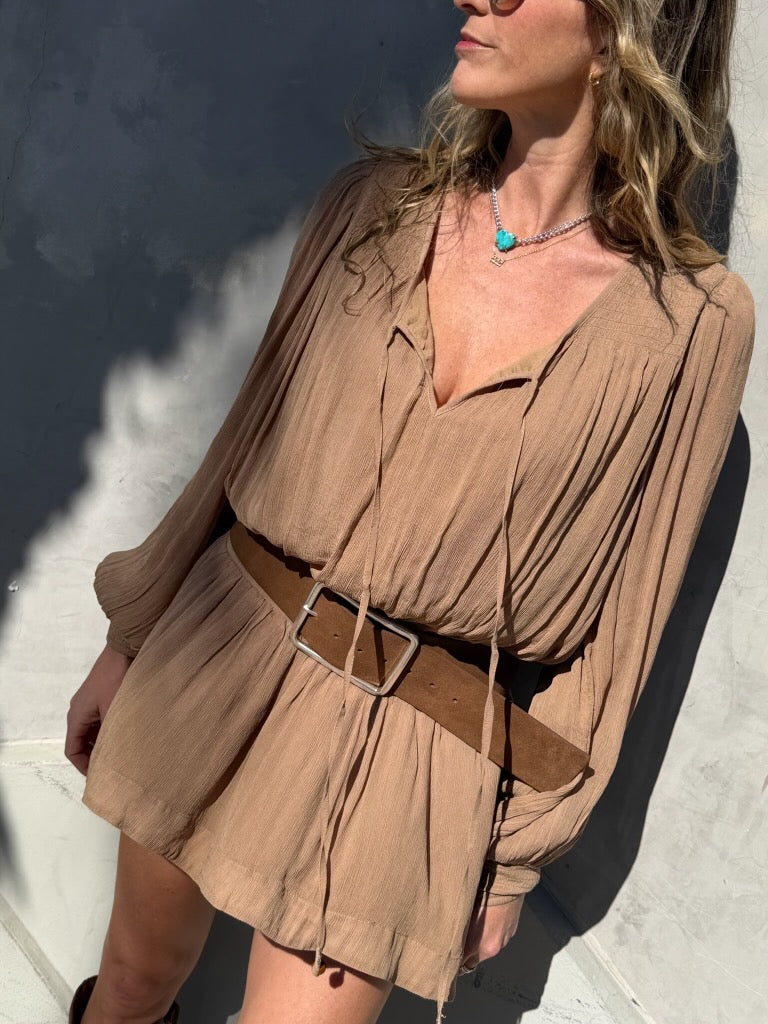 Woman wearing a tan mini dress, wide belt, turquoise necklace, and sunglasses outdoors in sunlight.