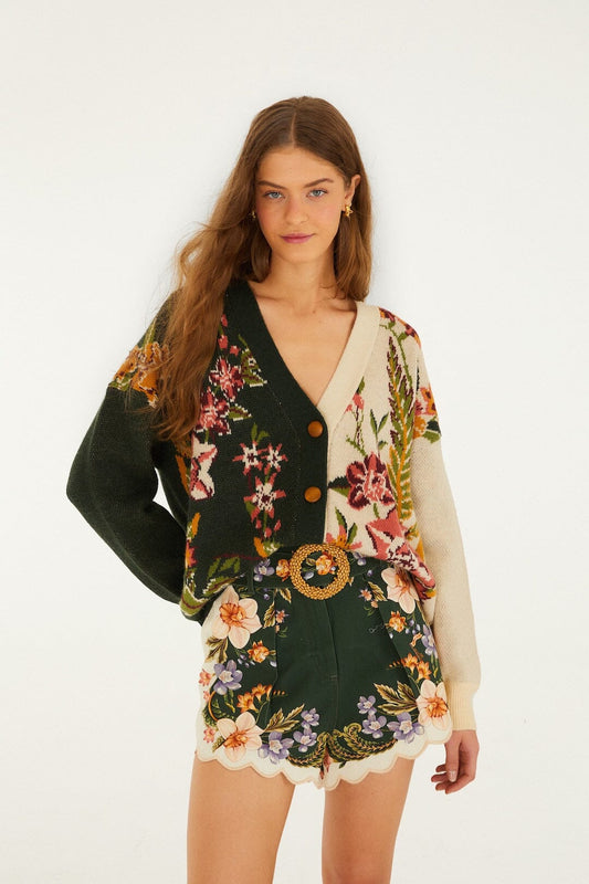 Woman wears sand-colored knit cardigan and high-waisted shorts with a botanical print, shown on white background.