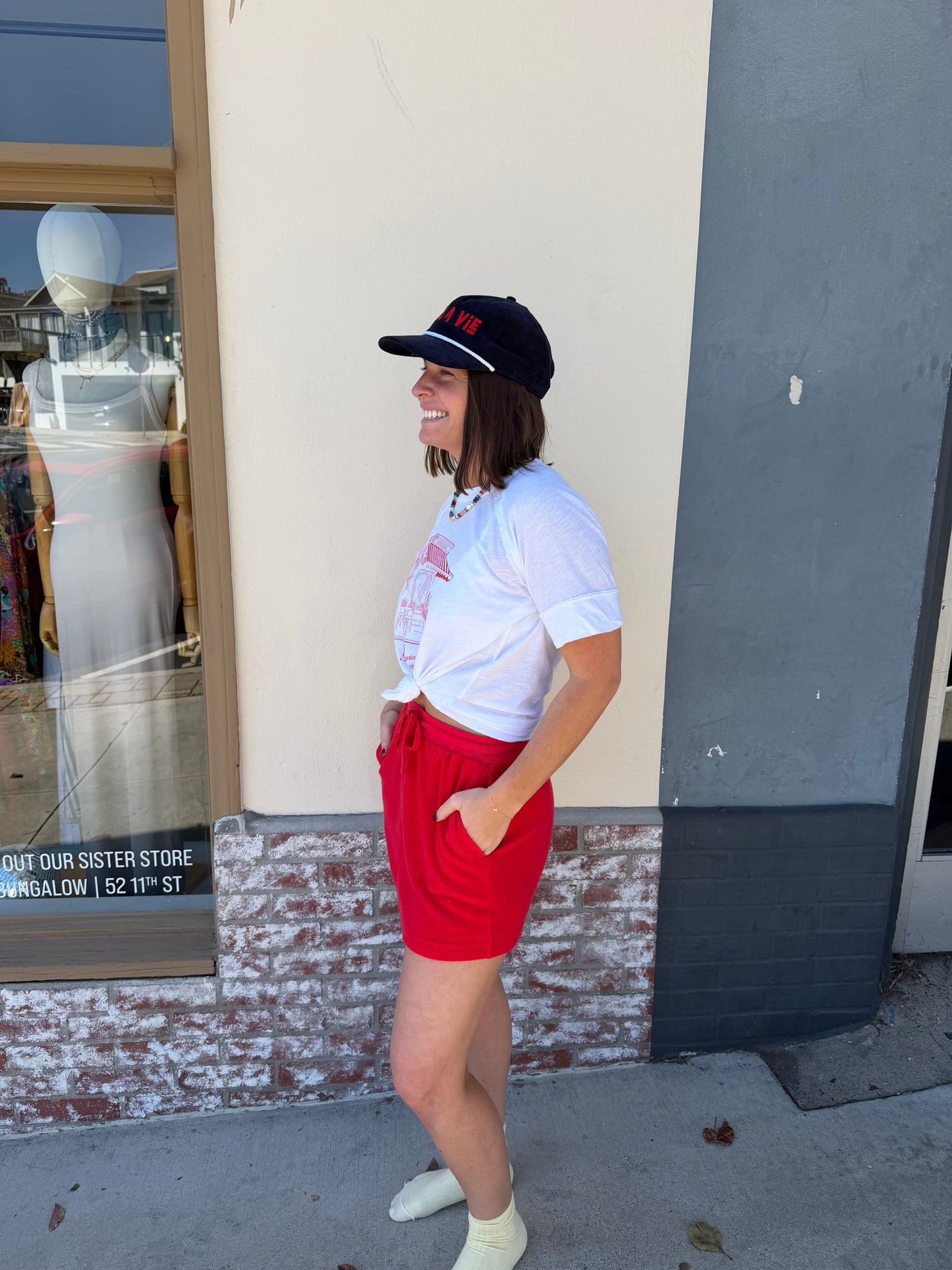 Woman wearing a white T-shirt and vermillion terry mini skirt stands outside, smiling with hands in her pockets.