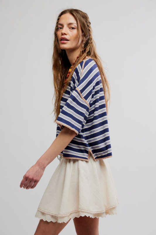 Woman in a blue and white striped top and tea-colored mini skirt, walking sideways with braided hair.