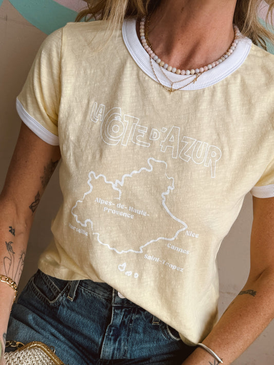 Woman wears a buttercream boxy ringer tee with jeans and beaded necklaces. Cotton material, casual use.