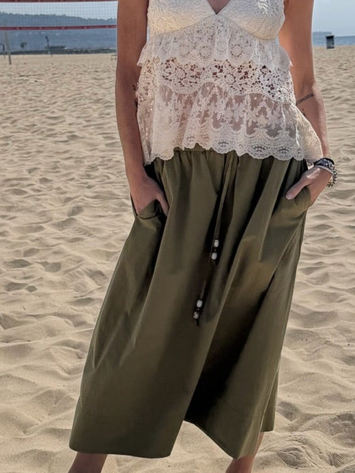 Person on sandy beach wearing a dark olive midi skirt with pockets, styled casually for relaxed outdoor wear.