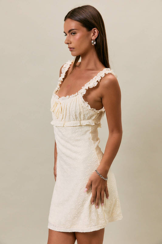 Woman wearing a white cotton mini dress with ruffled straps, shown in profile against a plain beige background.