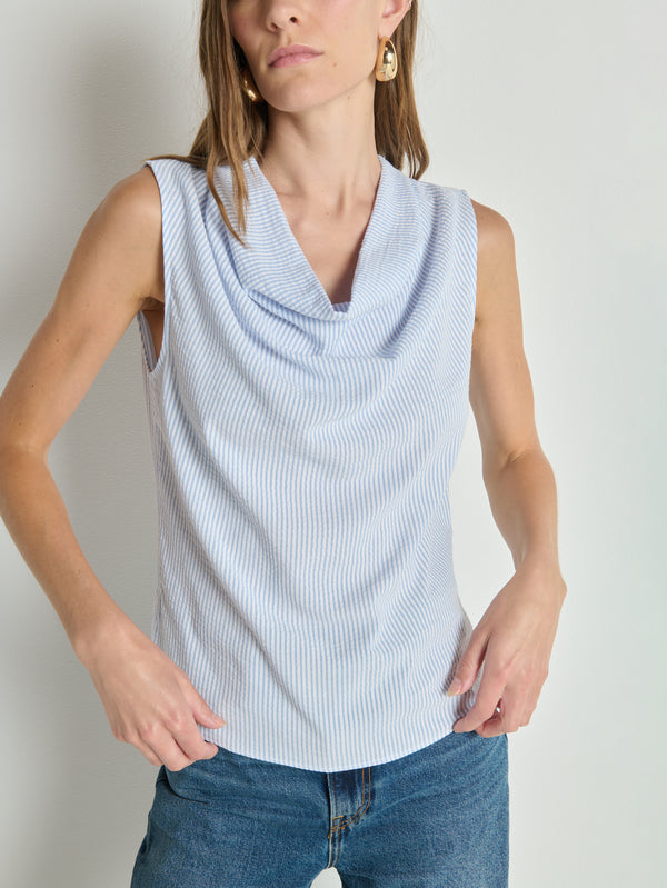 Woman wearing a mini stripe cowl neck tank top and blue jeans, standing against a plain white wall.