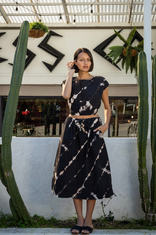 Woman in a tie-dye top stands between cacti outside a modern building. Cotton blend, casual wear.