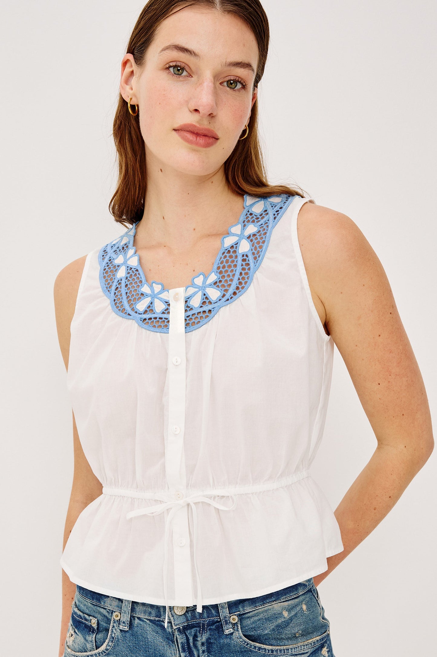 Woman wearing a white sleeveless top with blue embroidery