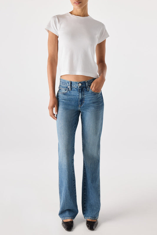 Individual in a white crop top and blue denim jeans, standing against a plain background.