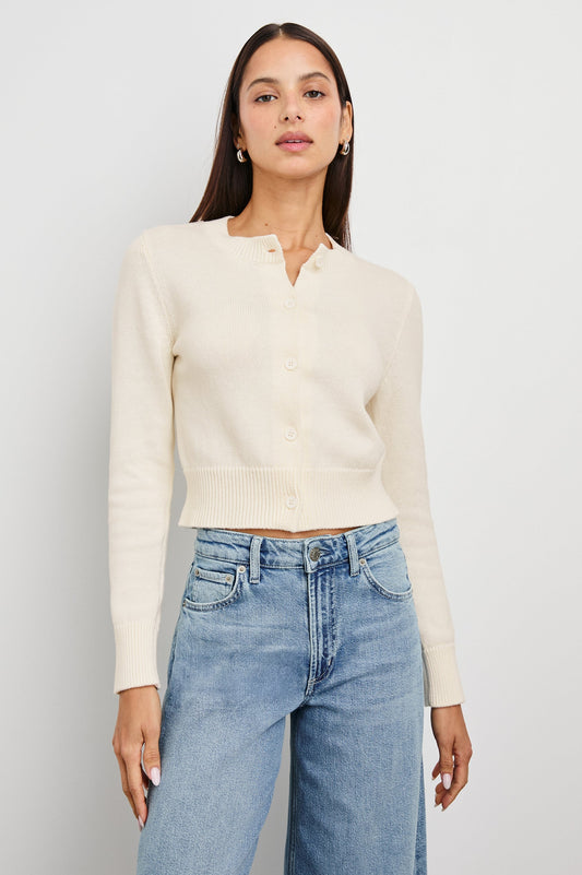Ivory knit cardigan and blue jeans, modeled by a woman standing against a plain white background.