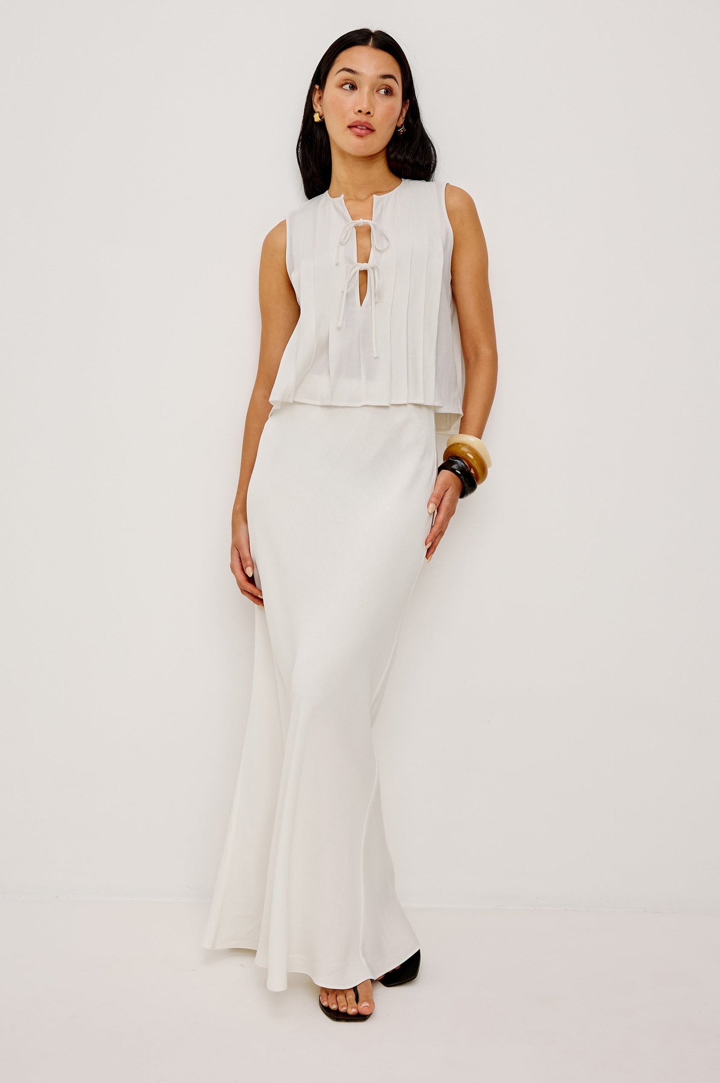 Woman in ivory midi skirt and sleeveless white tie-front top stands against a plain white background.