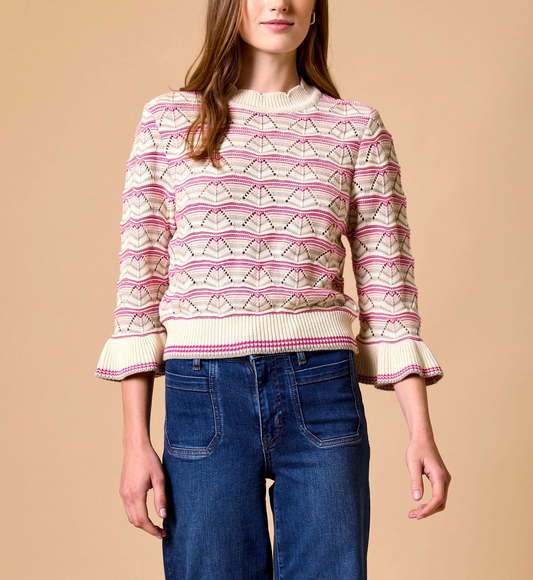 Ivory sweater with pink patterns and ruffle cuffs, paired with high-waisted blue jeans; suitable for casual wear.