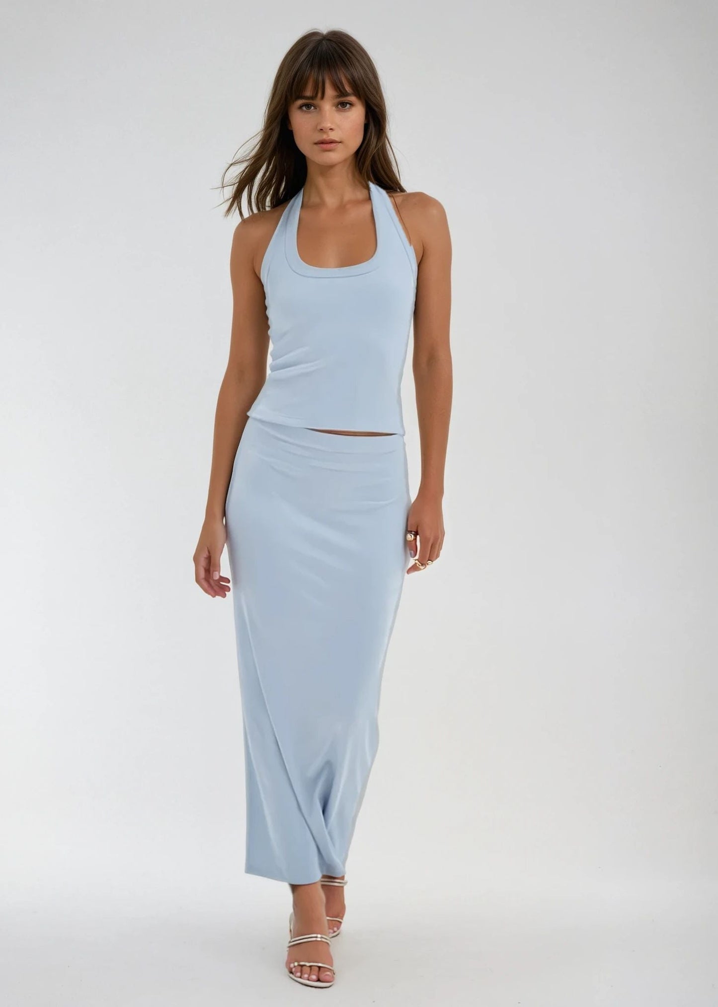 Woman in a light blue halter top and ribbed blue skirt, paired with strappy heels, standing against a plain background.
