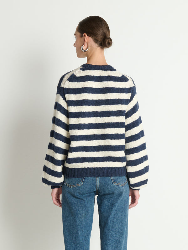 Back view of person in a blue-and-white striped knit cardigan and blue jeans on plain background.