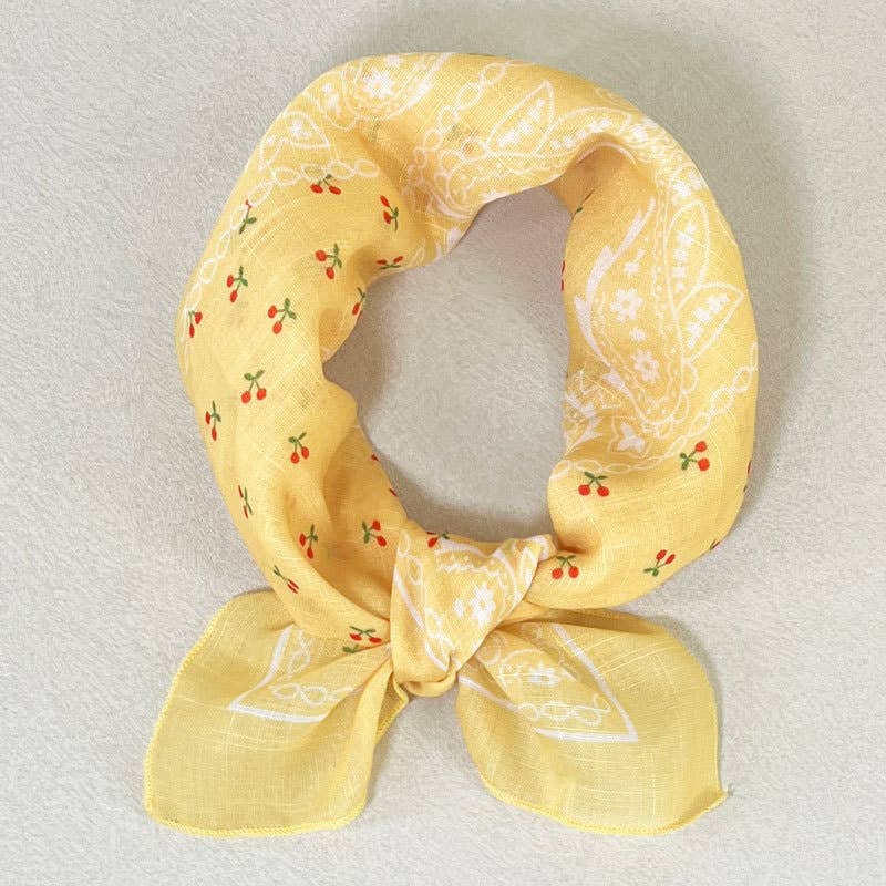 Red cotton bandana with cherry, white paisley, and yellow floral print; ideal as a multipurpose accessory.
