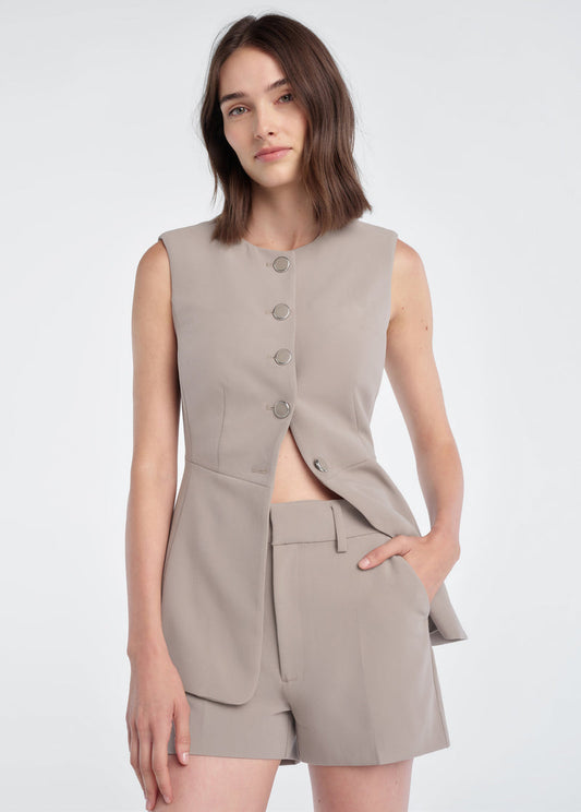 Woman in soft taupe mini shorts and a sleeveless blazer, showcasing tailored summer wear.