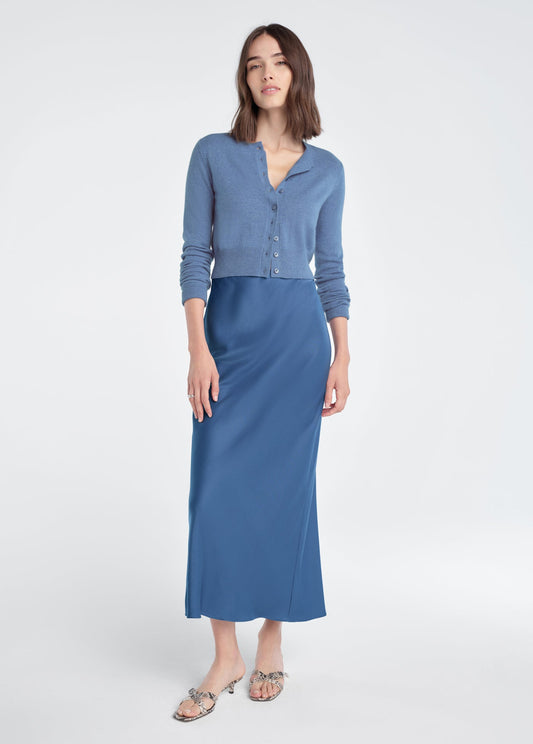 Woman wearing a river blue cropped cardigan and blue satin skirt, standing against a white background.