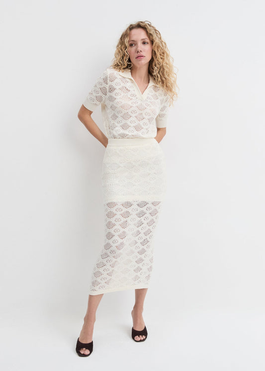 Woman with curly hair wears an ivory polo shirt, made of soft knit, suitable for casual or semi-formal occasions.