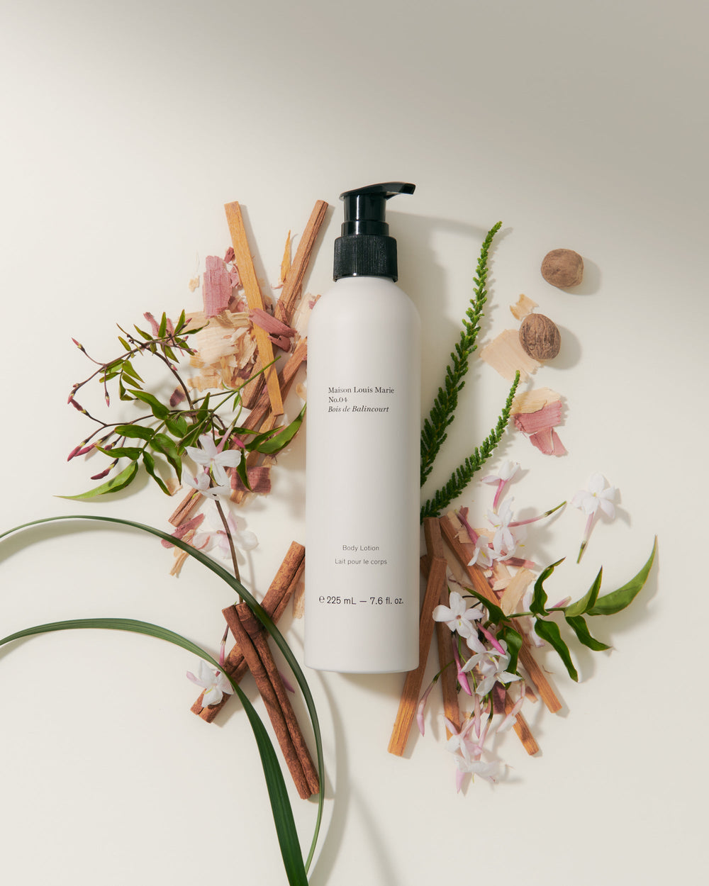 White plastic pump bottle of body lotion, placed among cinnamon sticks, flowers, and whole nutmeg.