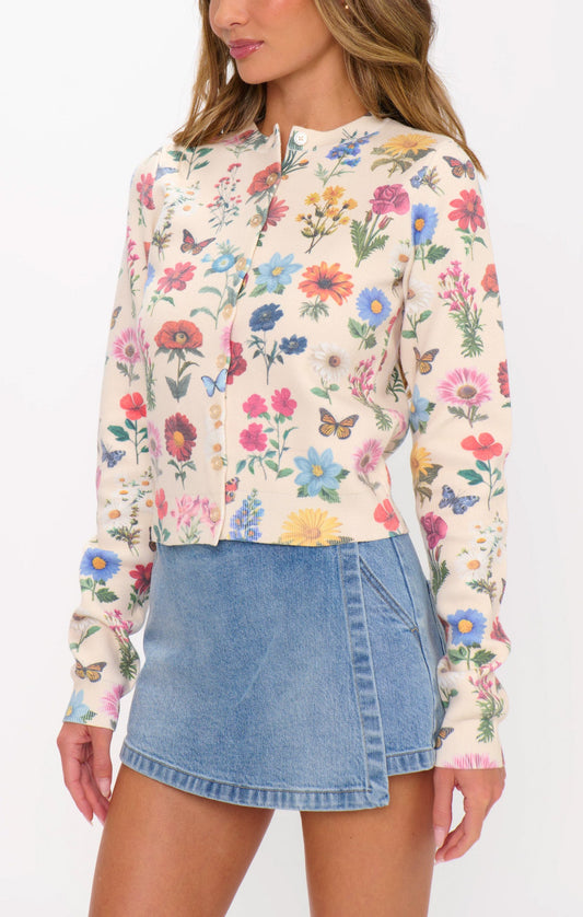 Woman wearing a French floral knit cardigan with a light blue asymmetrical denim mini skirt.