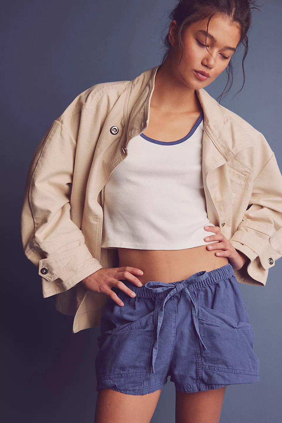 Woman wearing a beige jacket, white top, blue shorts