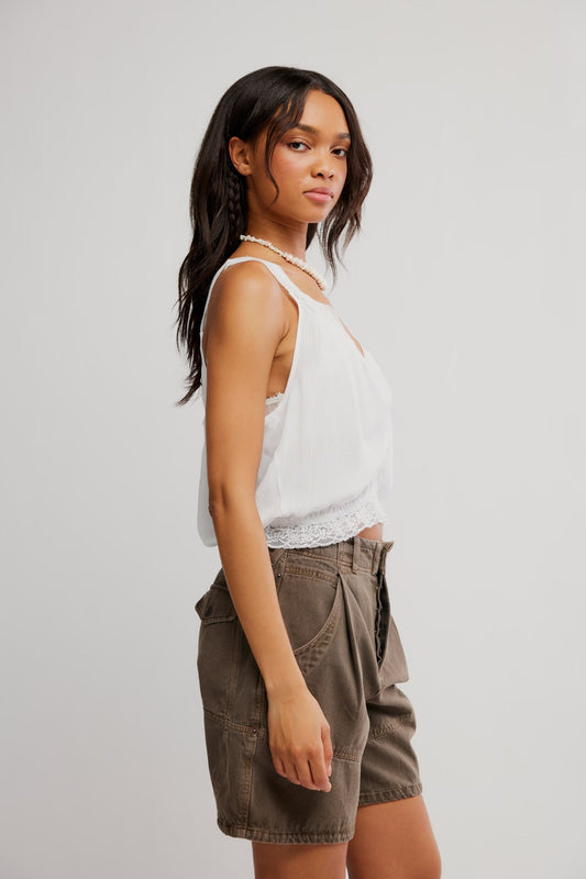 Woman wearing an ivory tank top and brown shorts, standing sideways against a light background.
