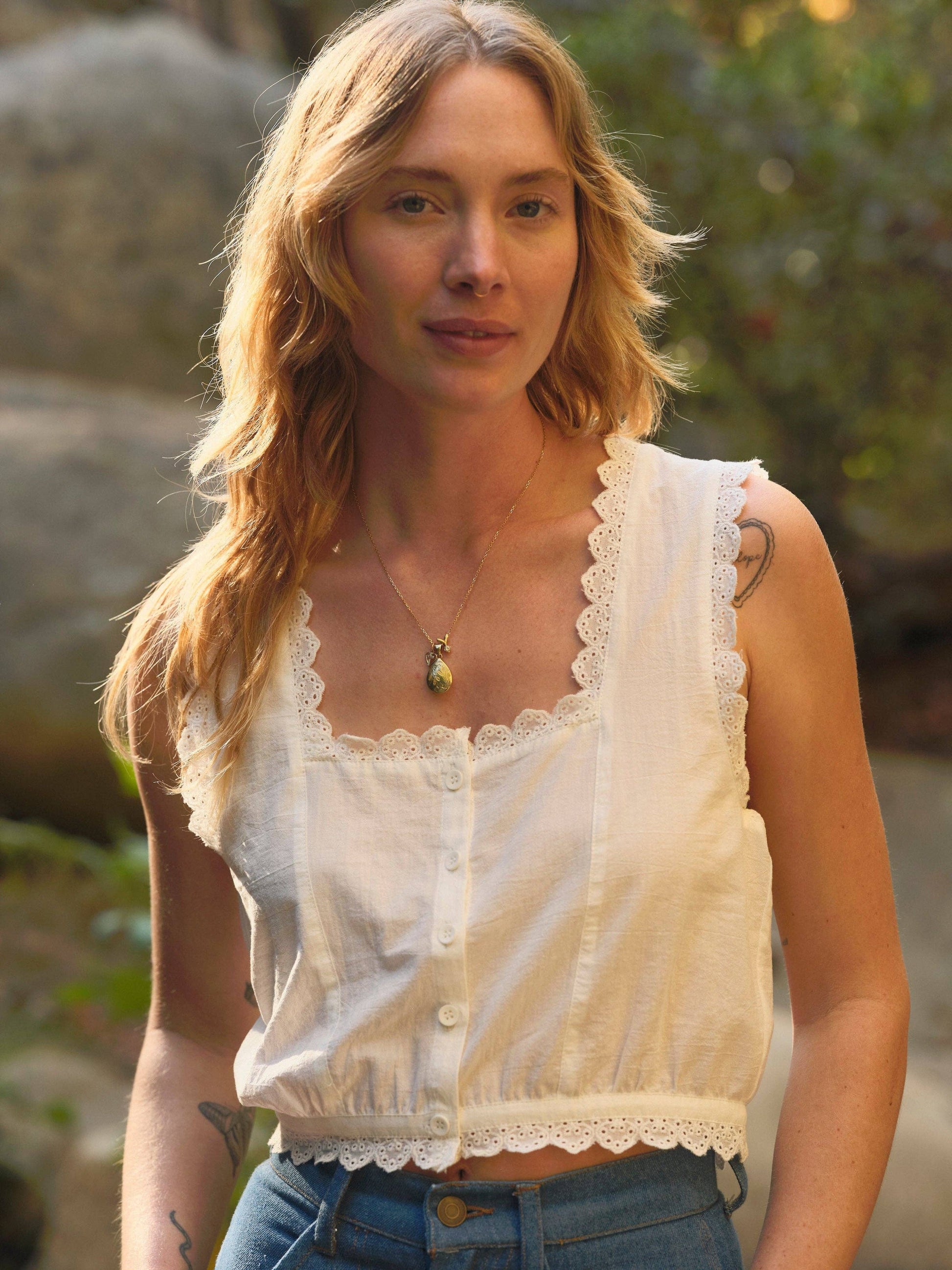 Woman in wavy blonde hair wears a white cotton top and blue jeans outdoors in sunlight.