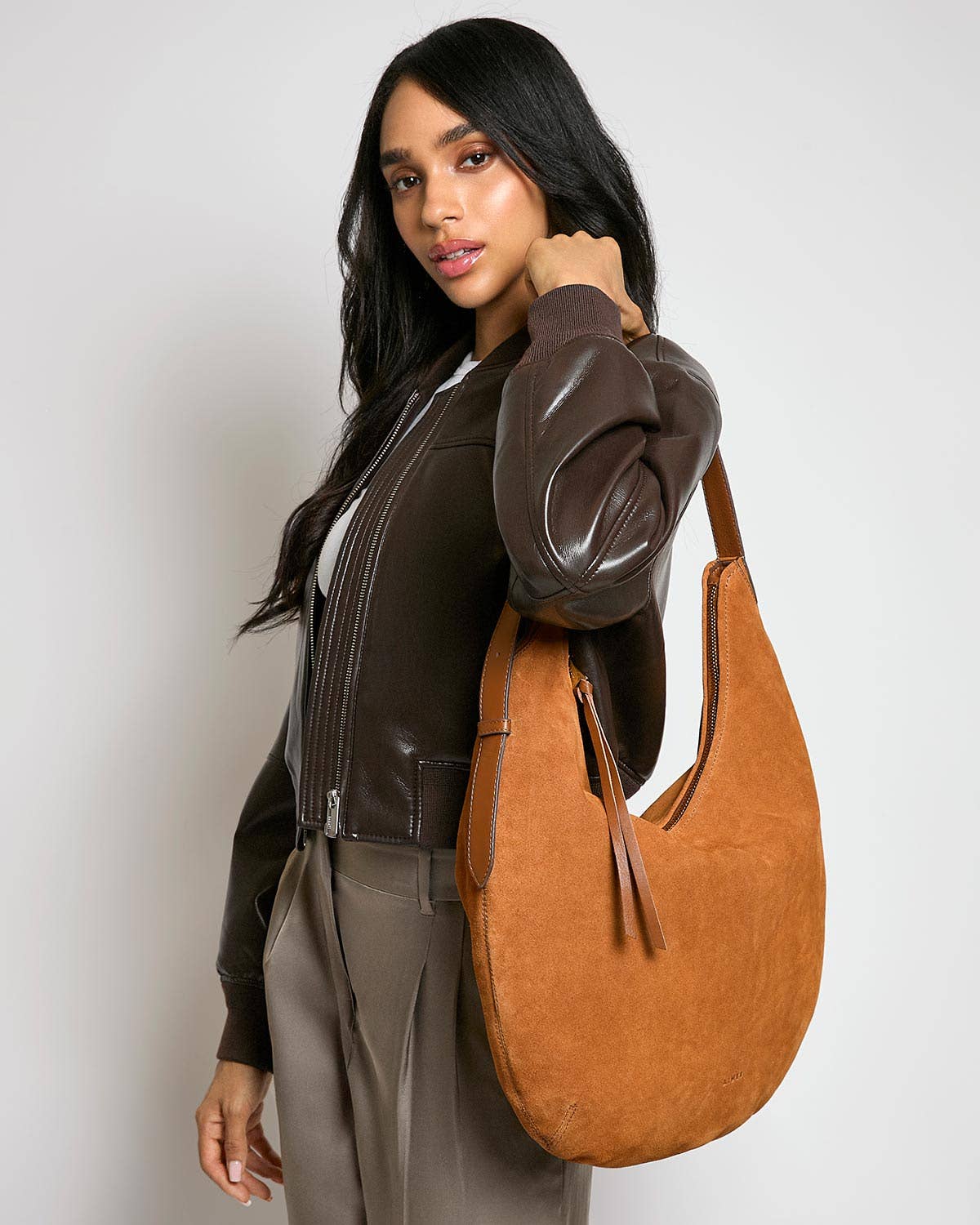 Woman with long dark hair holds a large black leather hobo bag, suitable for everyday use, against a simple background.
