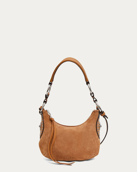 Latte suede mini crossbody bag with curved shape, bold strap, metal grommets, and a leather tassel.