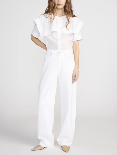 Model in a sleek black cape shirt, paired with high-waisted white wide-leg pants and beige pointed-toe shoes.