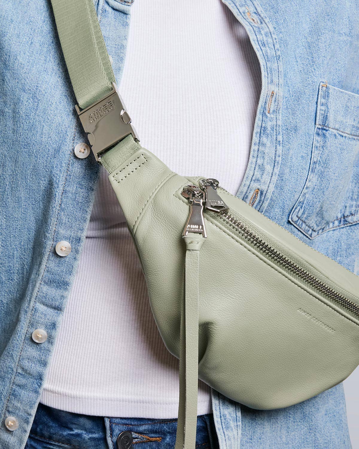 Tea Tree green sling bag with adjustable strap, worn over a white ribbed top and light blue denim jacket.