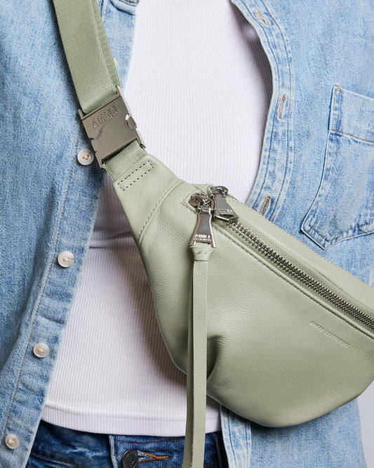 Tea Tree green sling bag with adjustable strap, worn over a white ribbed top and light blue denim jacket.