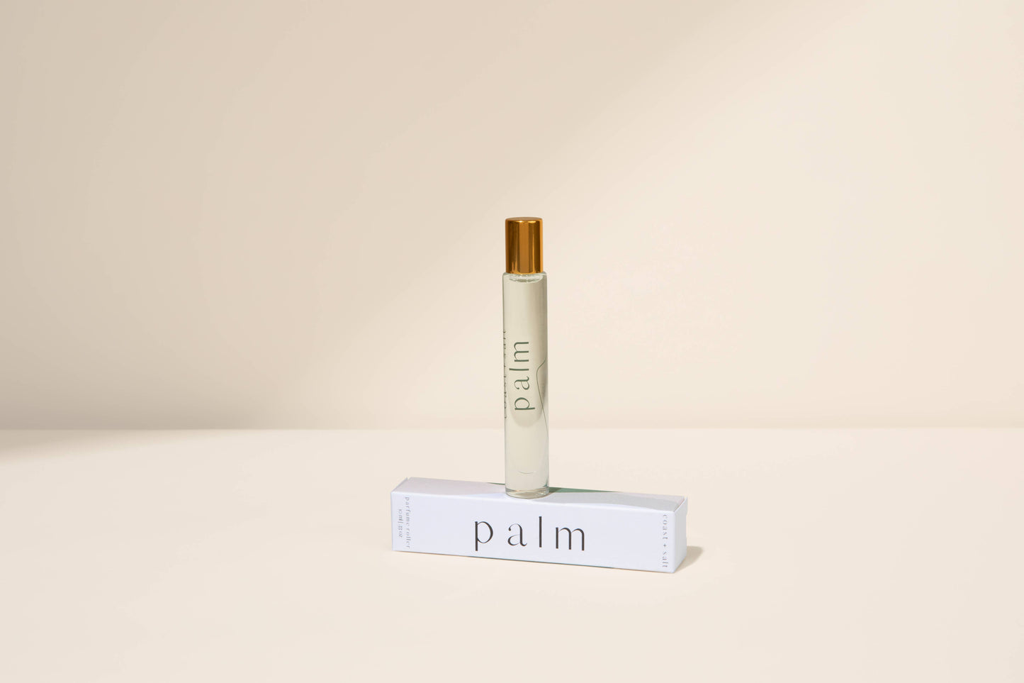 Palm perfume roller with gold cap placed on a white box, displayed against a beige background.