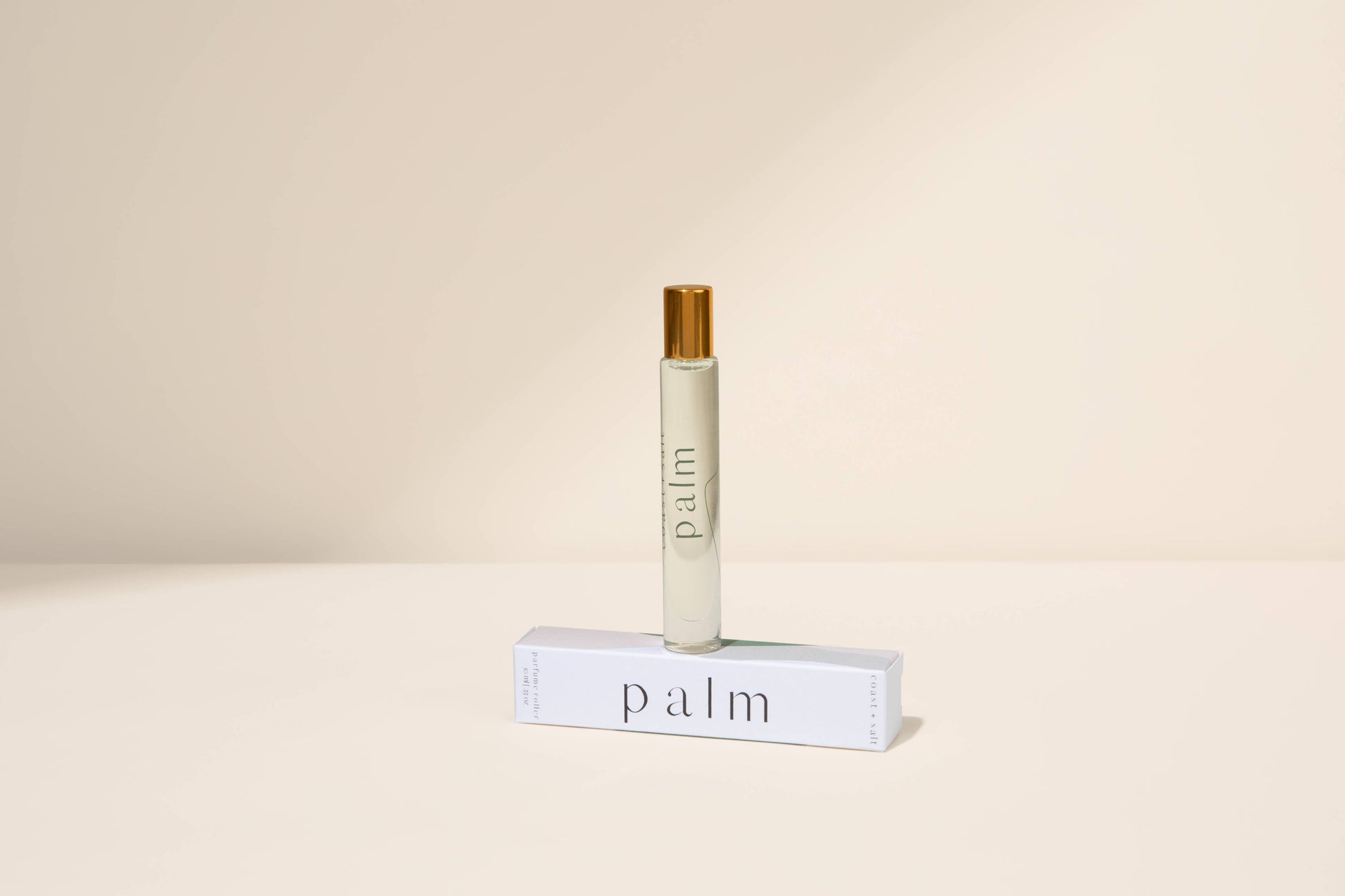 Palm perfume roller with gold cap placed on a white box, displayed against a beige background.