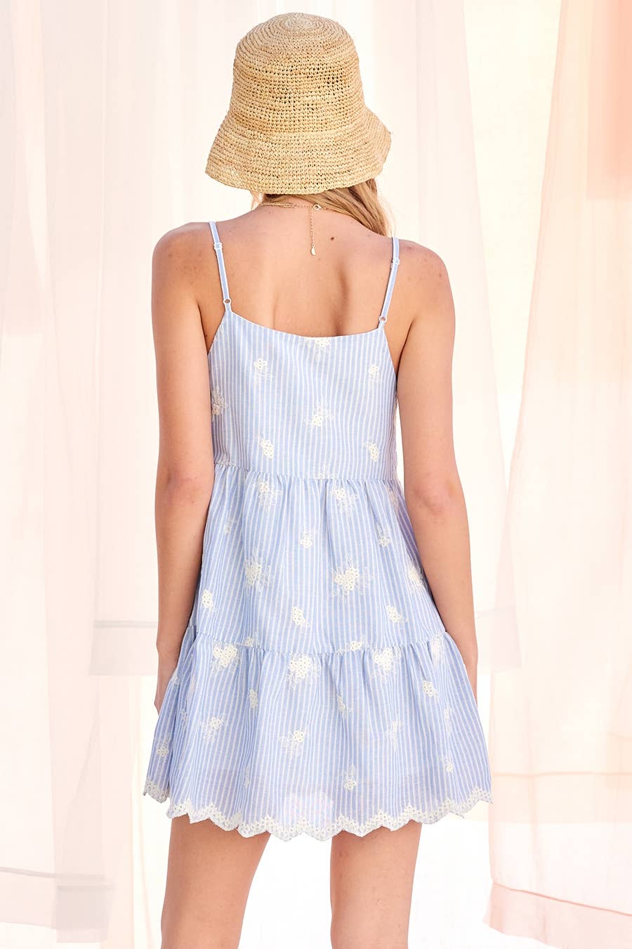 Back view of a woman in a light blue dress and straw hat, highlighting the dresss color and casual summer style.