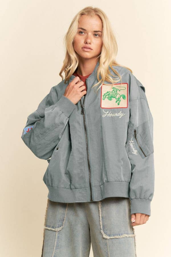 Woman wearing an embroidered bomber jacket with patches and light denim pants, suitable for casual wear.