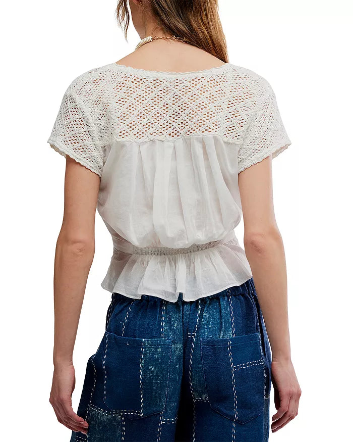 Back view of a woman wearing an ivory embroidered top and high-waisted denim patchwork jeans.