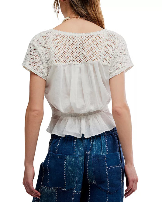 Back view of a woman wearing an ivory embroidered top and high-waisted denim patchwork jeans.