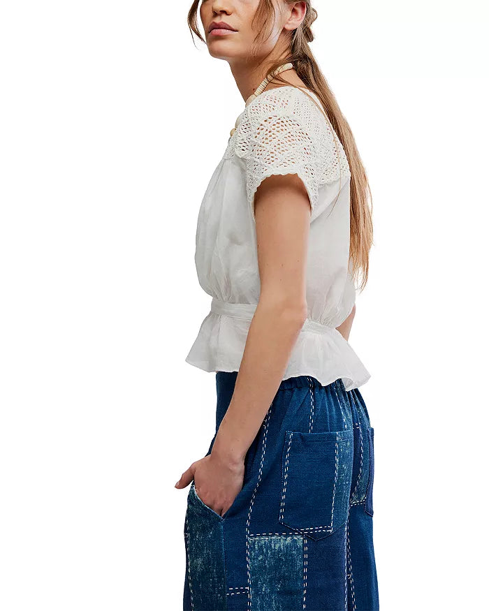 Woman wears an ivory embroidered top with a blue patchwork skirt, standing with hands in skirt pockets.