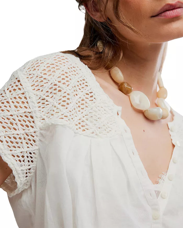 Woman in ivory embroidered cotton top with chunky beaded necklace, standing against a plain white background.