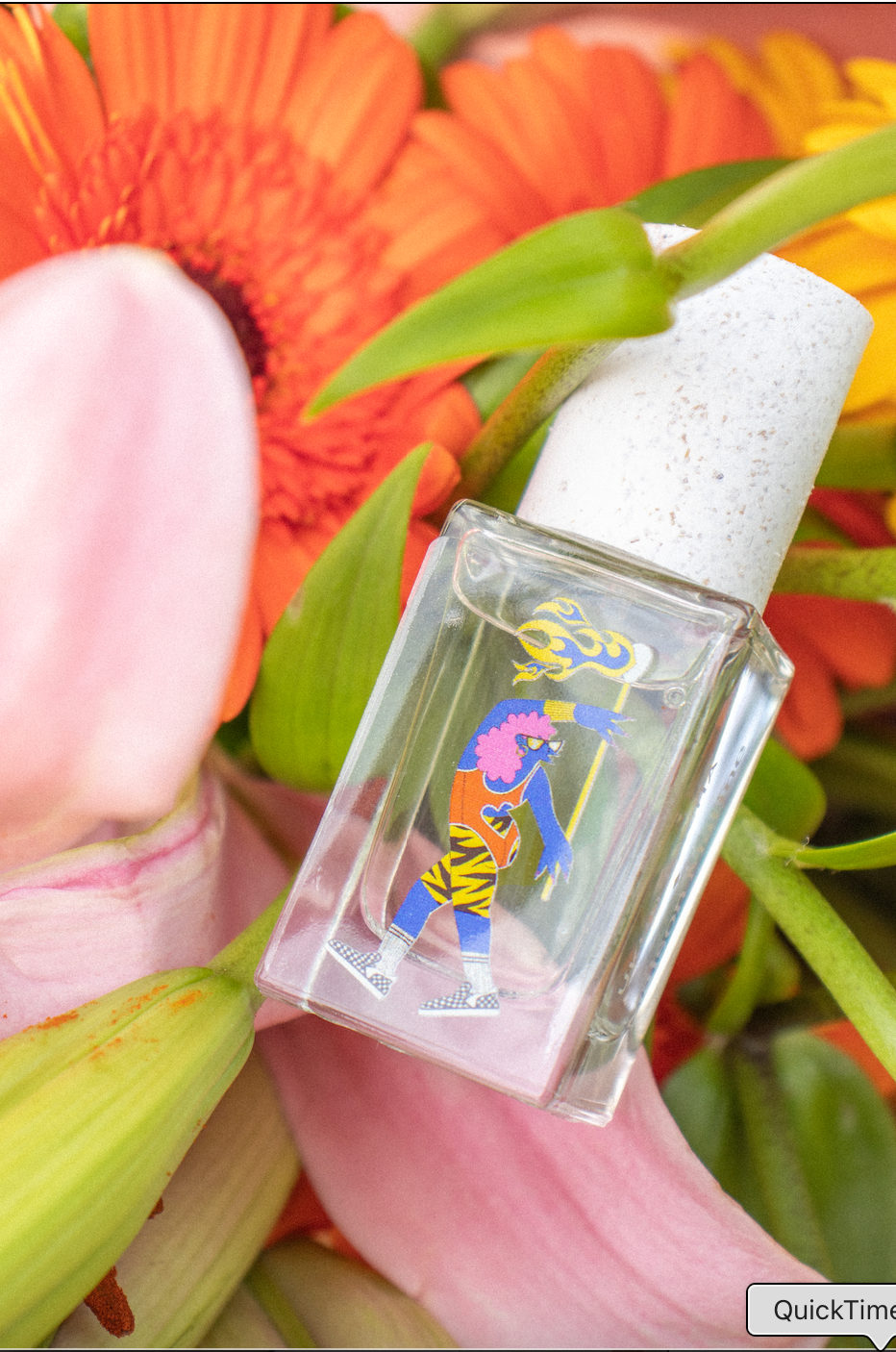 A 15ml perfume bottle with colorful design is placed among orange and pink flowers.