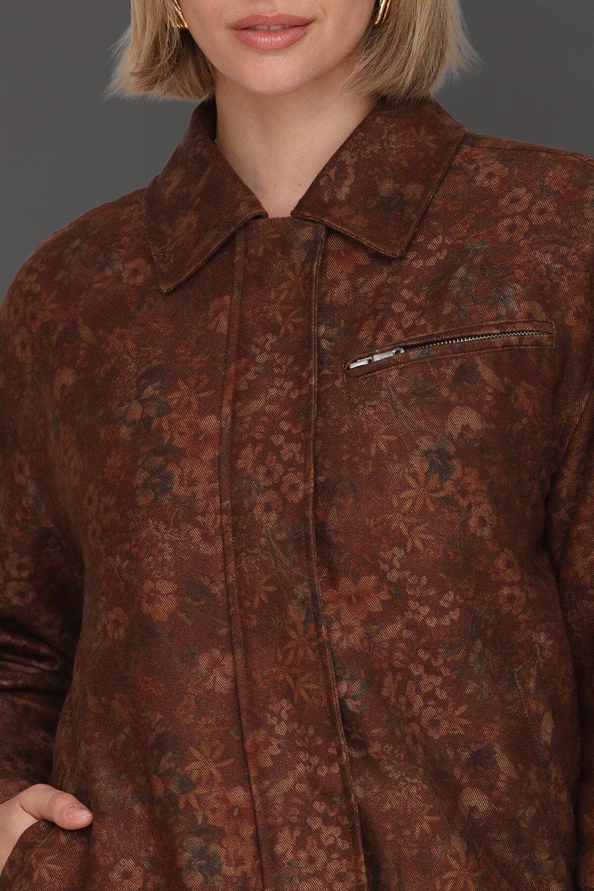 Woman in floral print bomber jacket with zip chest pocket, paired with gold hoop earrings.