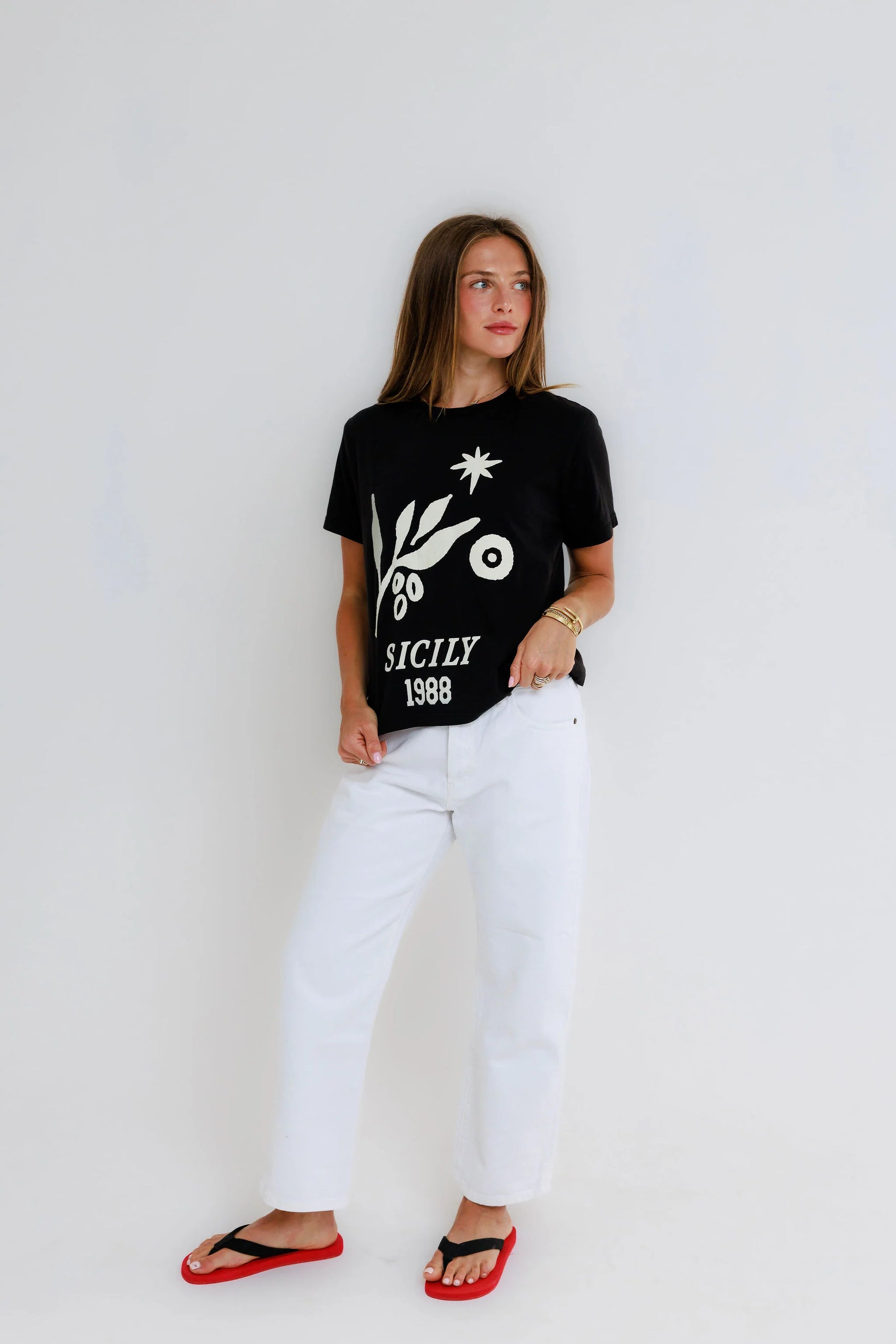 Woman wearing a black cotton tee, white pants, and red sandals against a plain white background.
