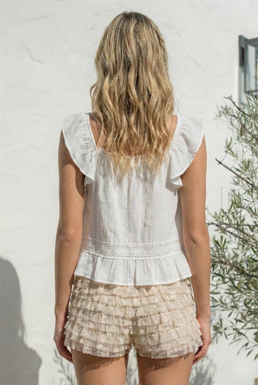 Woman with wavy blonde hair models a natural-colored ruffle sleeve top and matching shorts, shown from the back.