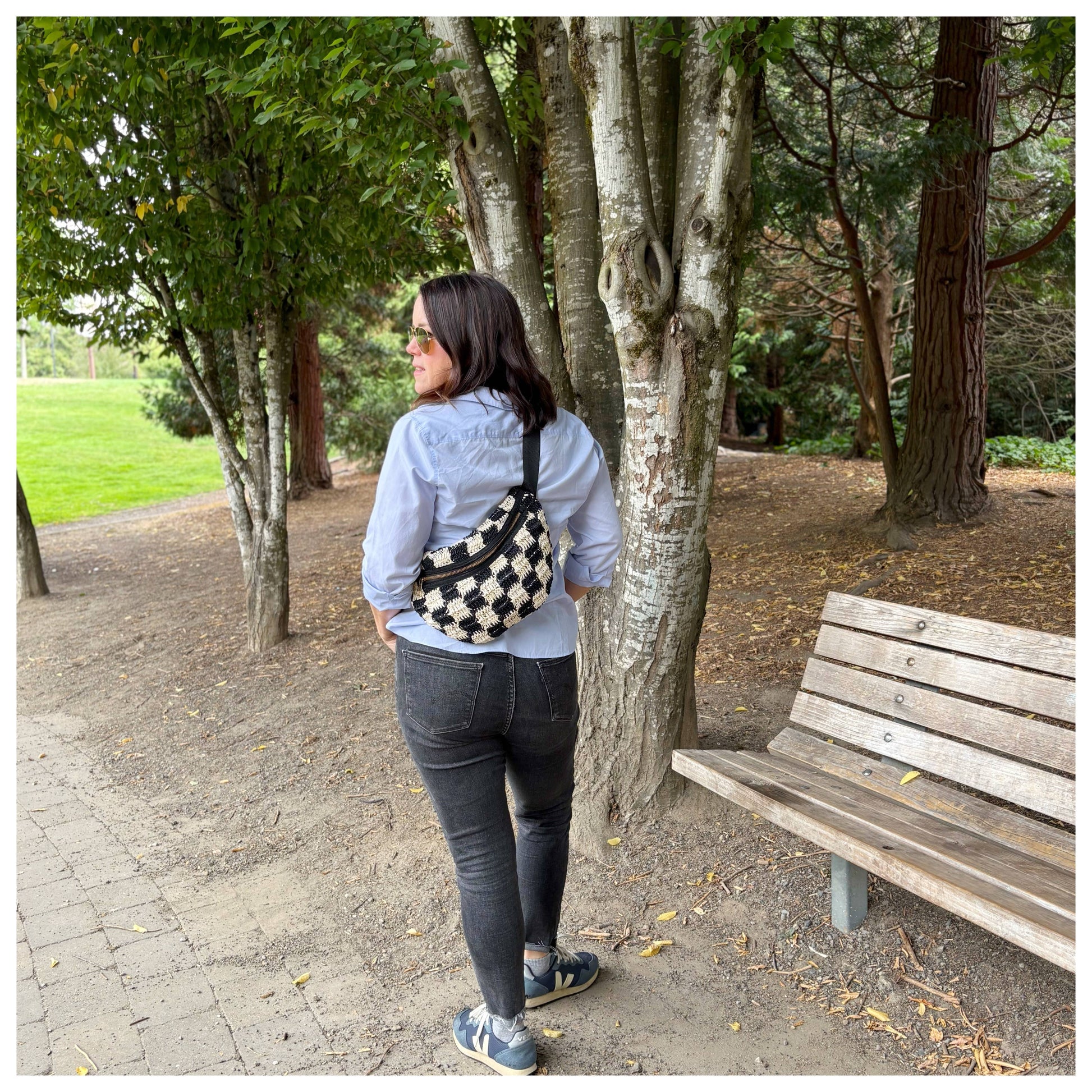 Person on a park path wears jeans, blue shirt, and a small checkered sling bag in canvas, worn across the body.