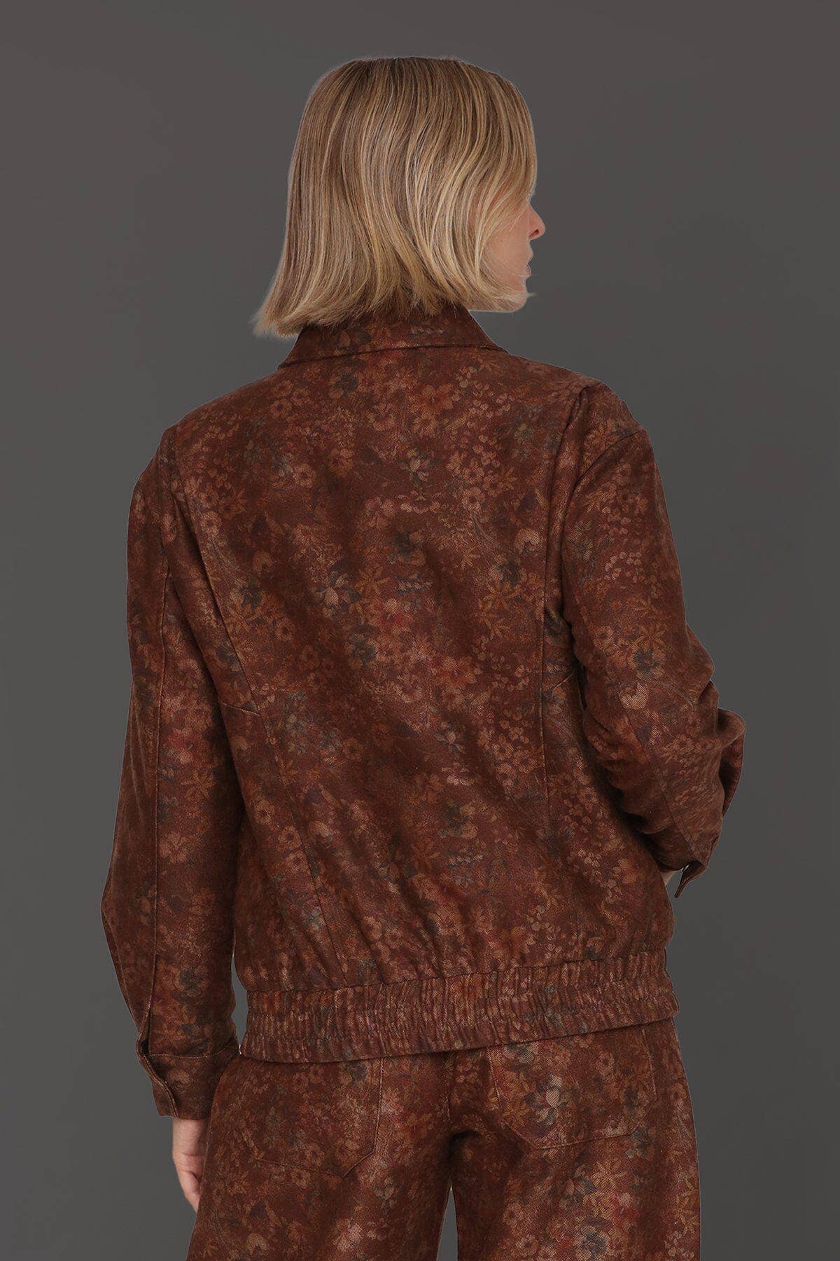 Person with chin-length blonde hair models a floral print bomber jacket in relaxed fit, shown from the back on a gray background.