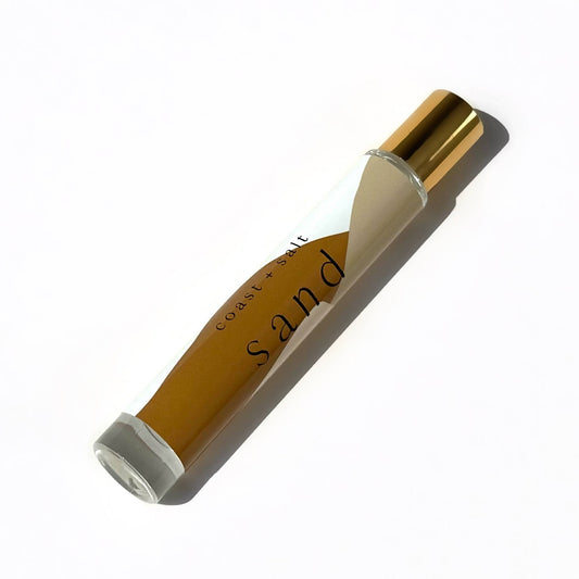 Coast+Salt Sand Perfume Roller with gold cap rests on a white surface; glass tube design for easy scent application.