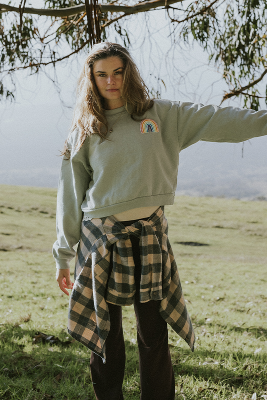 Woman wearing eucalyptus green cropped sweatshirt and plaid shirt at waist, standing on grass.
