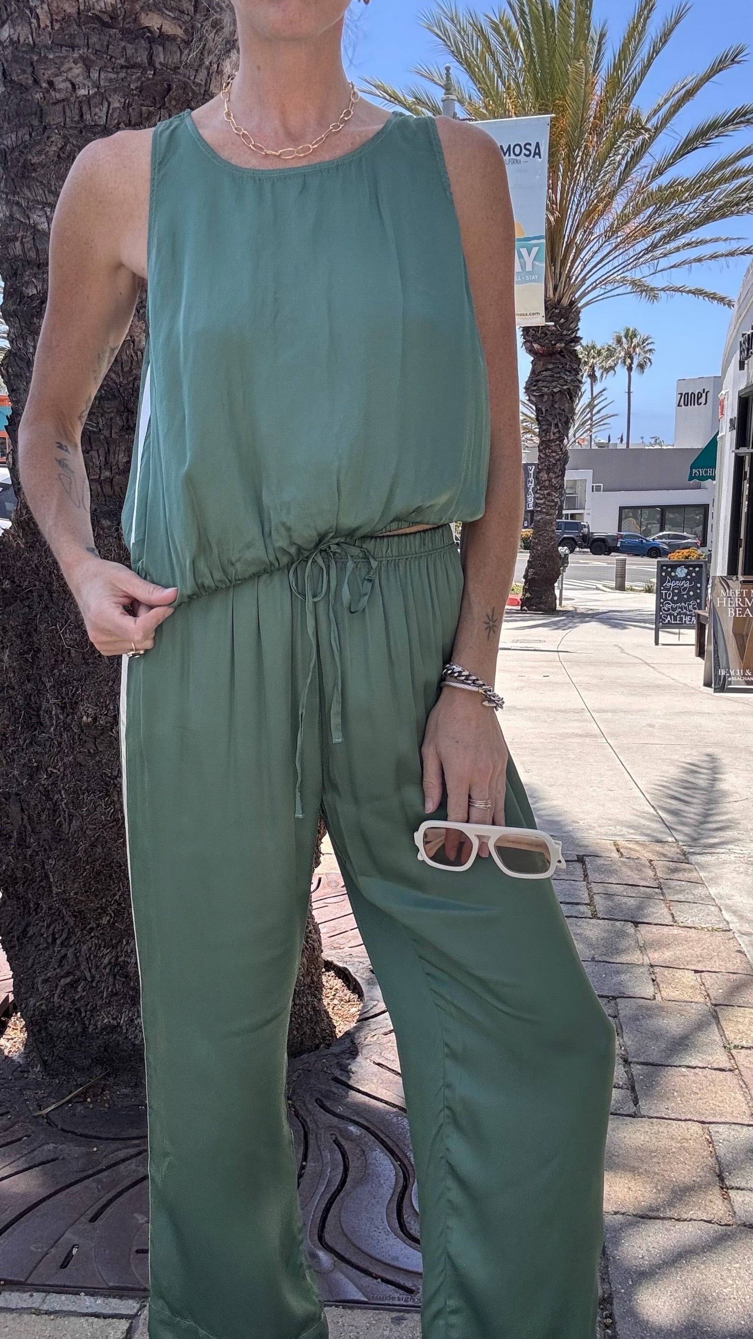 Caydn models celadon jade track pants, lightweight fabric, ideal for casual wear on a sunny sidewalk with palm trees.