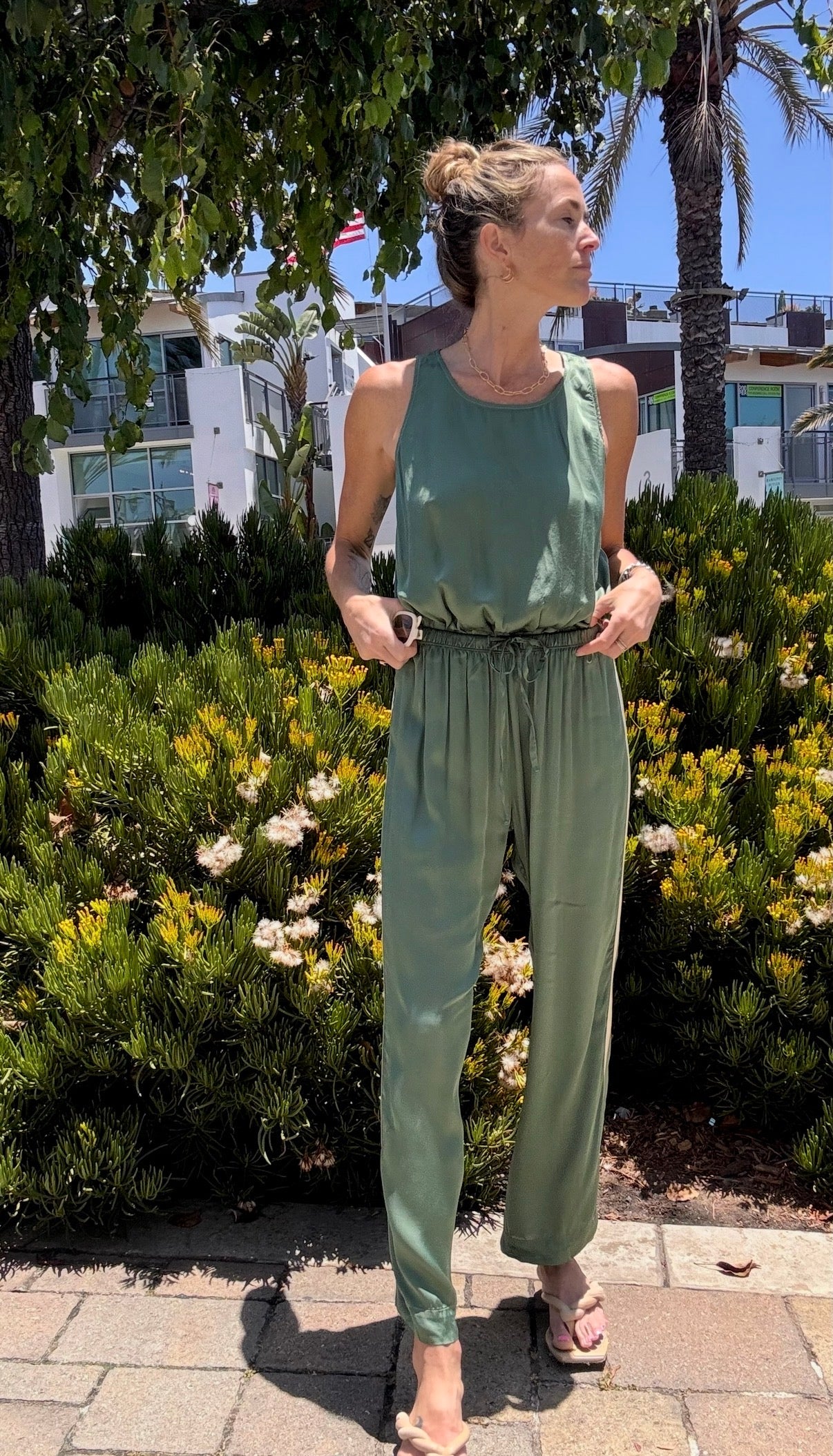 Person wears Celadon Jade track pants outdoors amid greenery and palm trees on a sunny day.