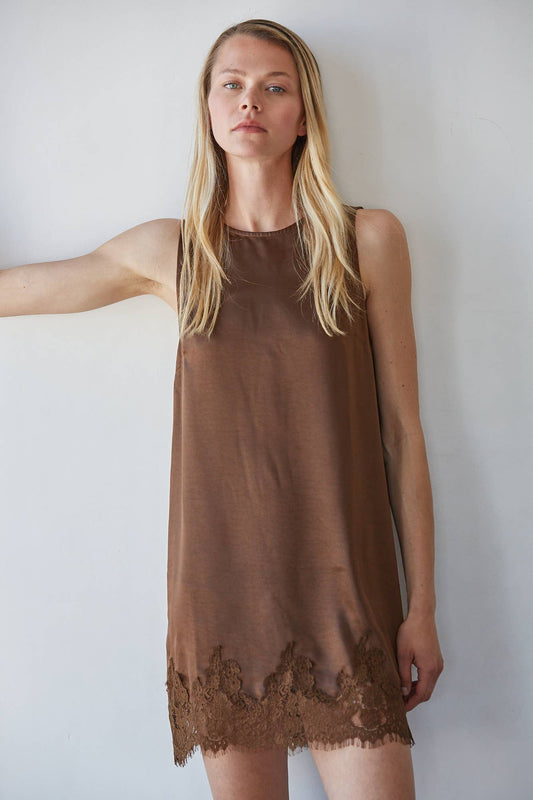 Woman in a brown lace-trim mini dress, standing against a white wall. Dress is lightweight, suitable for casual wear.