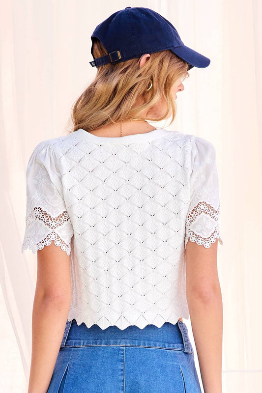 Back view of woman wearing off-white cardigan, navy cap, lace v-neck top, and blue jeans.